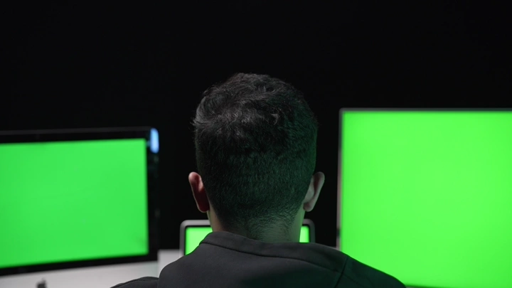 رجل يعمل على شاشات كروما خضراء في مكتب مظلم، لقطة خلفية.