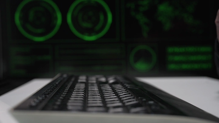 لوحة مفاتيح أمام شاشات خضراء، لقطة مقرّبة.