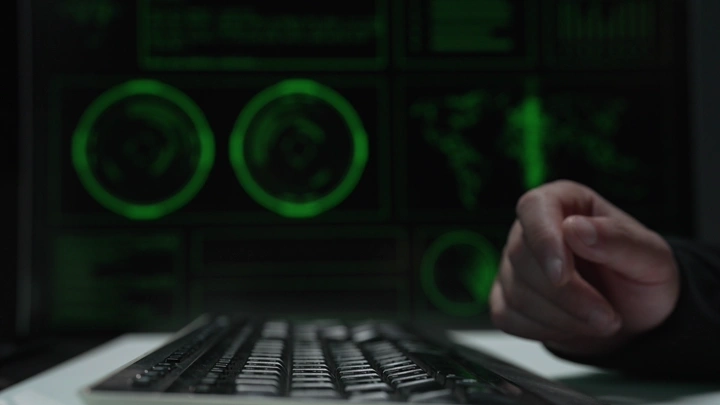 يد تكتب على لوحة مفاتيح أمام شاشة بيانات، لقطة قريبة.