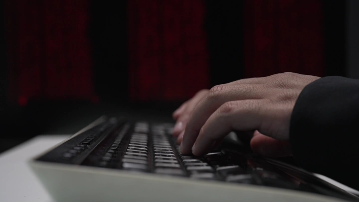 يد تكتب على لوحة مفاتيح في بيئة مظلمة، لقطة مقربة.