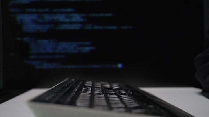لوحة مفاتيح أمام شاشة بها كود برمجي، لقطة قريبة.