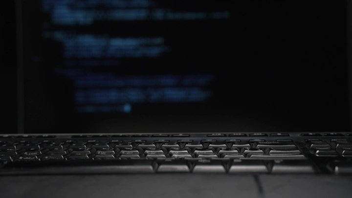 لوحة مفاتيح أمام شاشة تعرض كود برمجي، لقطة مقربة.