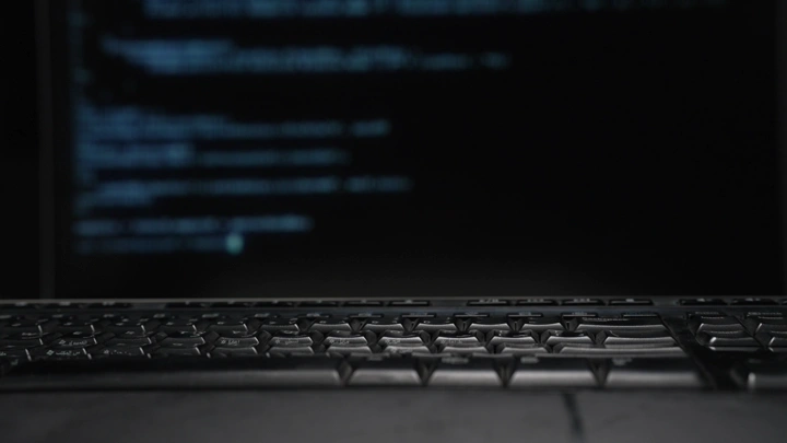 لوحة مفاتيح أمام شاشة تعرض كود برمجي، لقطة قريبة.