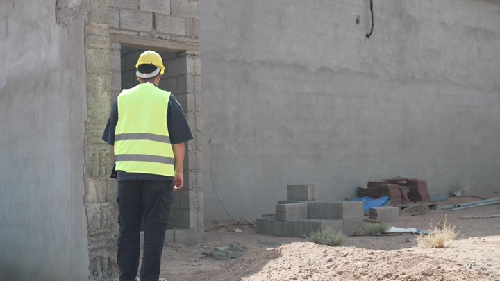مهندس يرتدي سترة صفراء وخوذة في موقع بناء، لقطة من الخلف.