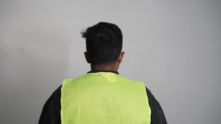 رجل يرتدي سترة صفراء واقية، لقطة من الخلف.