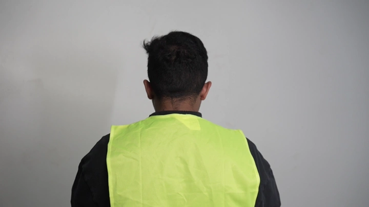 رجل يرتدي سترة أمان صفراء في غرفة، لقطة خلفية.