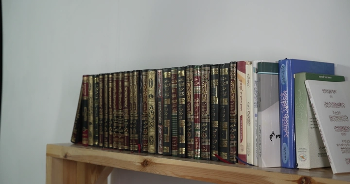 مجموعة كتب على رف خشبي في غرفة، لقطة داخلية.