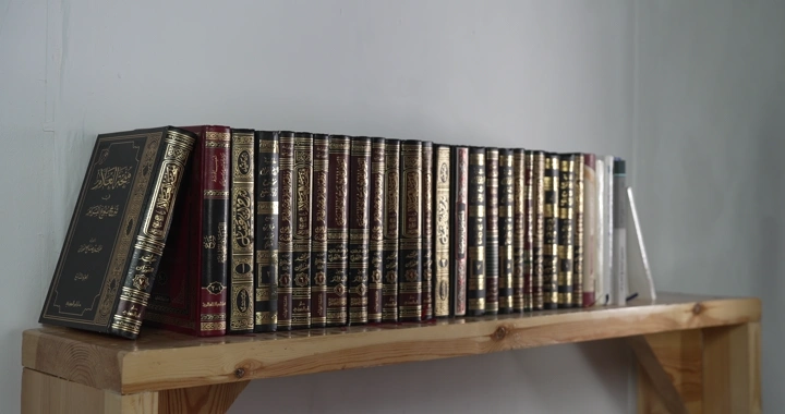 رجل يأخذ من مجموعة كتب على رف خشبي في غرفة مضاءة، لقطة جانبية.