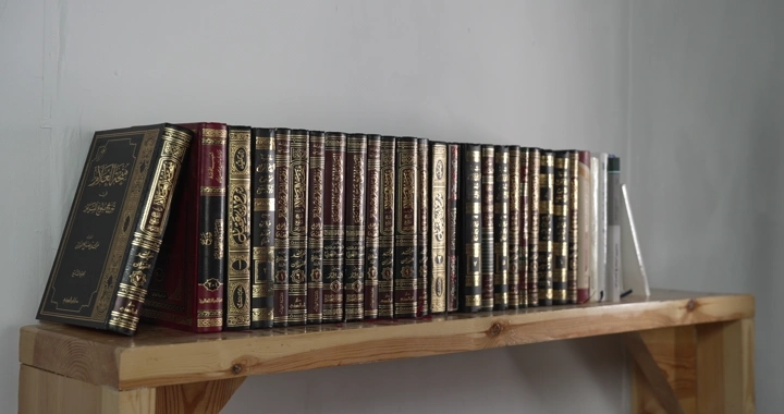 رجل يختار من مجموعة كتب مرتبة على رف خشبي في غرفة، لقطة ثابتة.