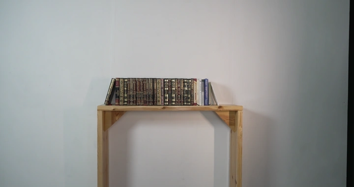 رف خشبي عليه كتب في غرفة بيضاء، لقطة ثابتة.