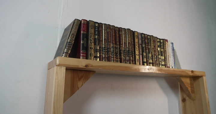 مجموعة كتب على رف خشبي، لقطة داخلية.