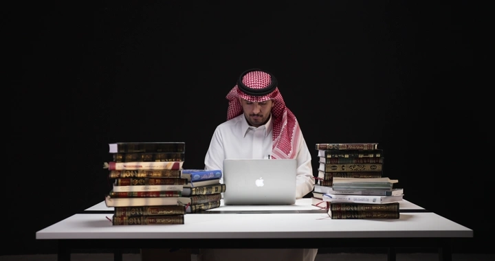 رجل يعمل على الكمبيوتر بين الكتب، لقطة واسطة.