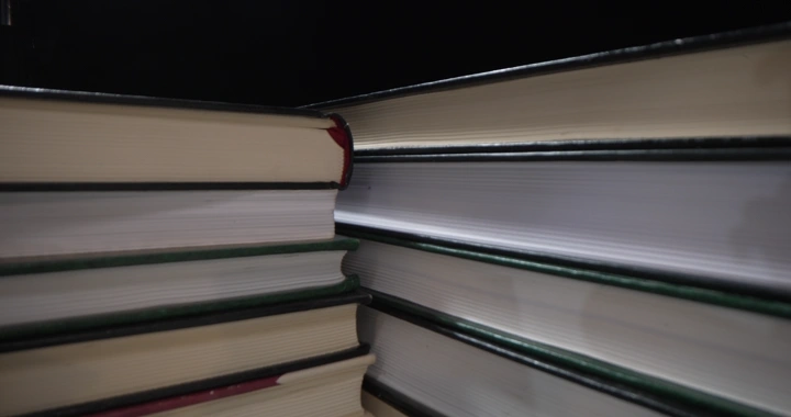 كتب مكدسة على مكتب في إضاءة خافتة، لقطة قريبة.