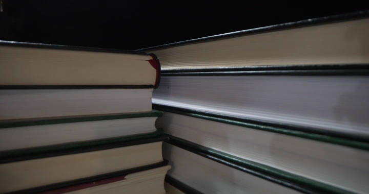 كتب مكدسة على مكتب في إضاءة خافتة، لقطة قريبة.