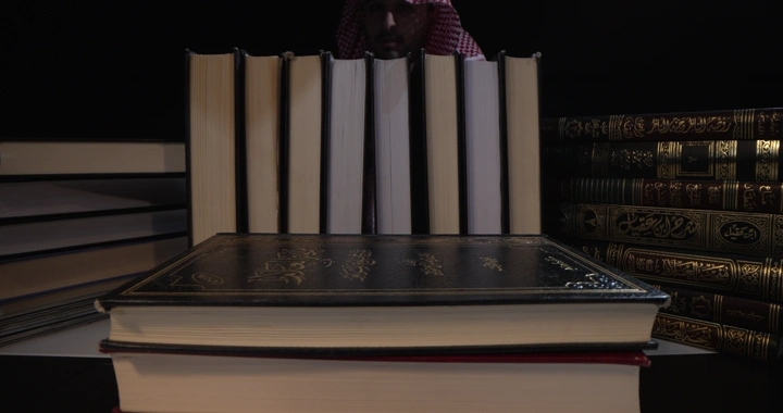 كتب مرتبة على رف في مكتبة مع رجل يقرا ، لقطة داخلية.