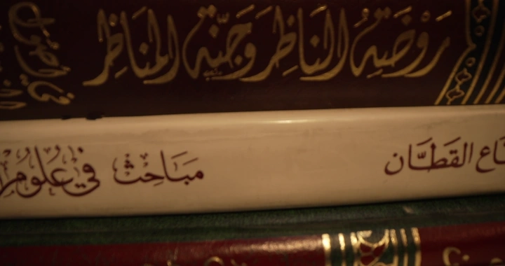 كتب عربية مكدسة مع إضاءة دافئة وشخص يكتب على للوحة مفاتيح، لقطة قريبة.