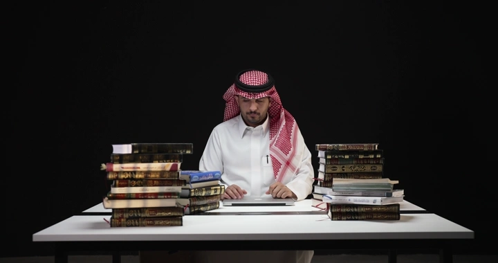 رجل يجلس بين كتب على طاولة بيضاء، لقطة امامية.