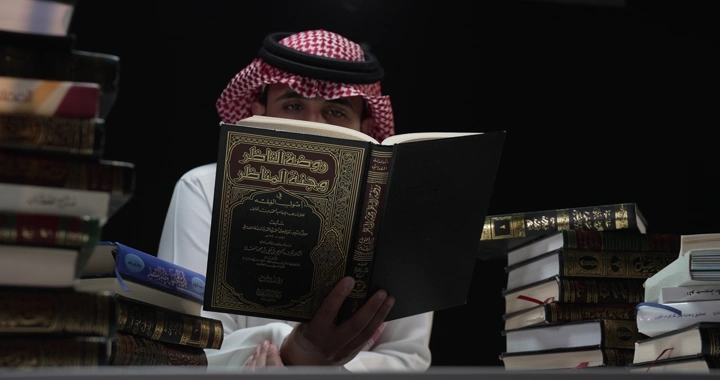 رجل يقرأ كتابًا بين مجموعة من الكتب، لقطة داخلية.