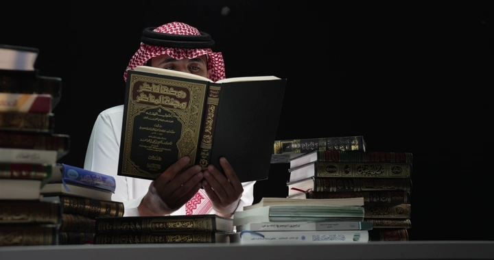 رجل يقرأ بين كتب على طاولة، إضاءة خافتة.