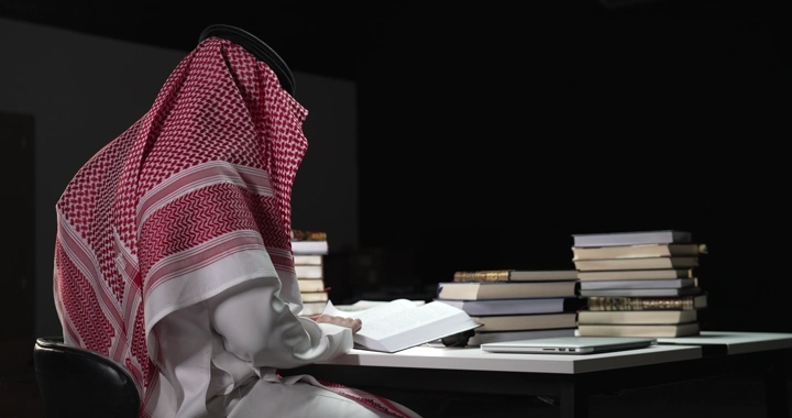 رجل يرتدي الزي التقليدي يقرأ بين الكتب، لقطة داخلية.