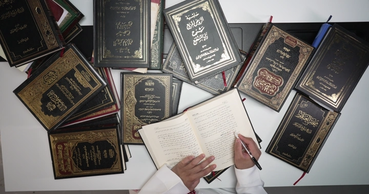 رجل يقرأ بين كتب إسلامية على مكتب، لقطة علوية.