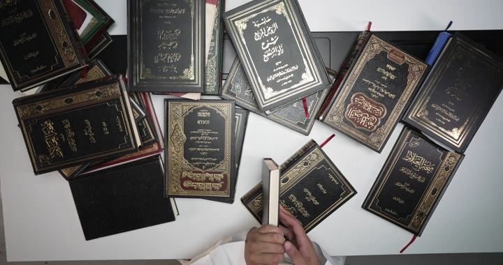 رجل يقرأ بين كتب إسلامية على طاولة، لقطة علوية.