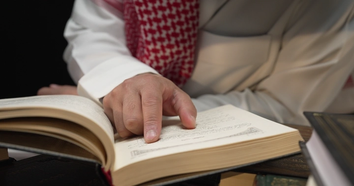 رجل يرتدي ثوبًا يقرأ كتابًا، لقطة مقربة.