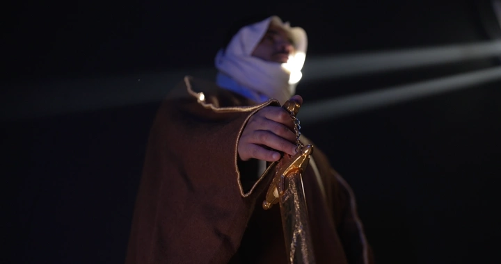 رجل يرتدي بشت ويمسك سيفًا في إضاءة درامية، لقطة منخفضة.