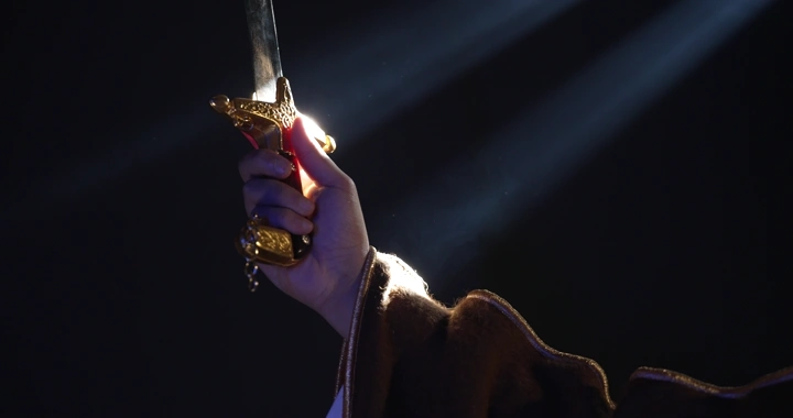 يد ترفع سيفًا تحت ضوء مسلط، لقطة درامية.