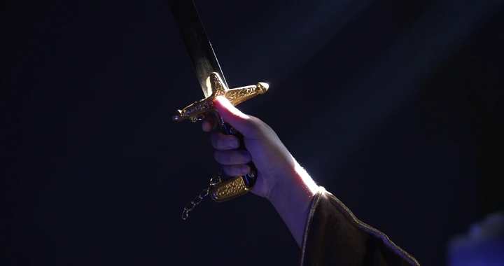 يد ترفع سيفًا ذهبيًا في الظلام، لقطة قريبة.