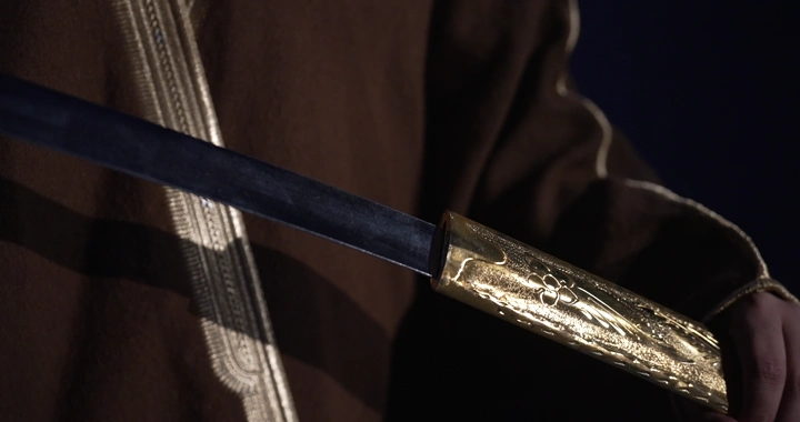 رجل يرتدي بشت يحمل سيفًا مزخرفًا، لقطة مقربة.