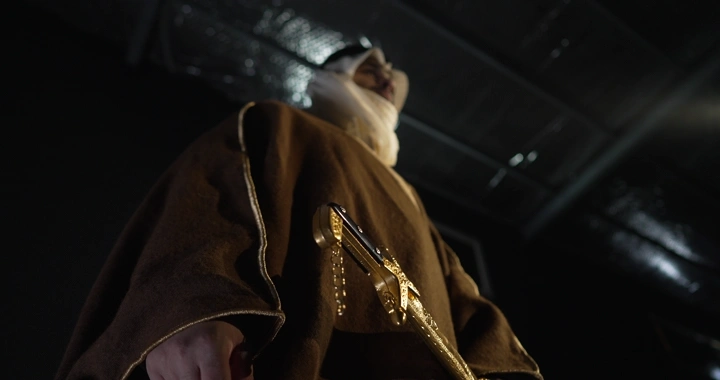 رجل يرتدي عباءة تقليدية يحمل سيفًا ذهبيًا، زاوية منخفضة.