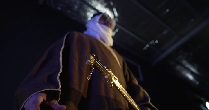 رجل يرتدي بشت  تقليدية يحمل سيفًا ذهبيًا، لقطة من الأسفل.