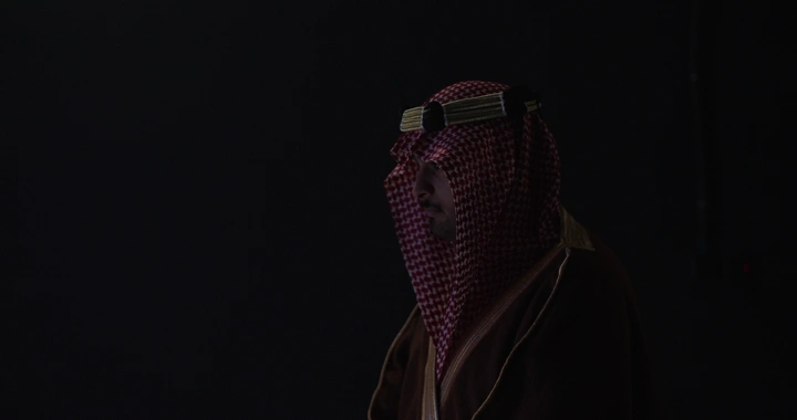 رجل يرتدي بشت وغترة في إضاءة خافتة، لقطة جانبية.