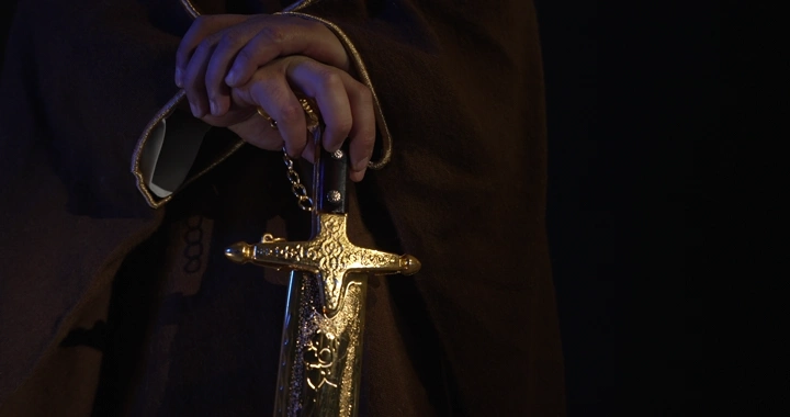 رجل يرتدي بشت يمسك سيفًا ذهبيًا، لقطة مقربة.