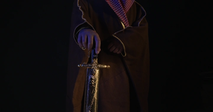 رجل يرتدي بشت ويمسك سيفًا، إضاءة خافتة.