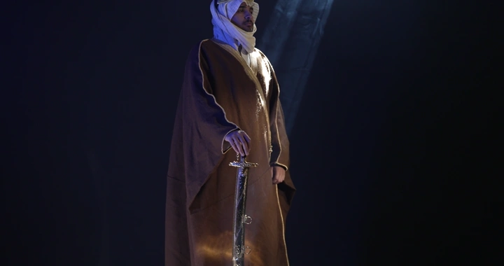 رجل يرتدي بشت ويمسك سيفًا في إضاءة سينمائيه.