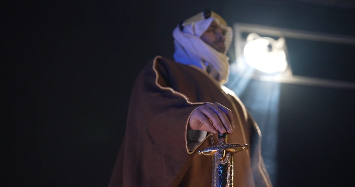 رجل يرتدي عقالًا ويمسك سيفًا، إضاءة درامية.