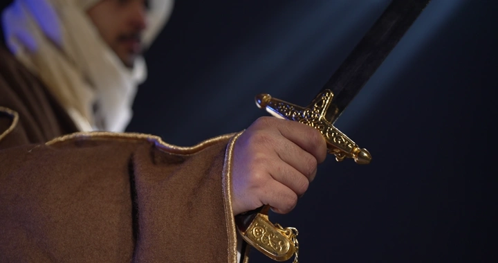 رجل يرتدي بشت يمسك سيفًا مزخرفًا، لقطة مقربة.