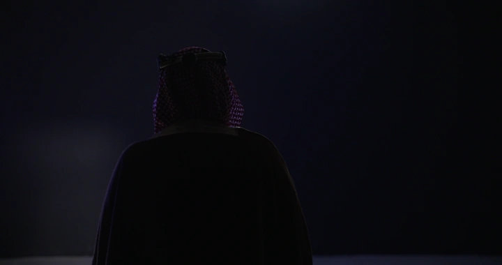 رجل يرتدي بشت وعقال في إضاءة خافتة، لقطة خلفية.