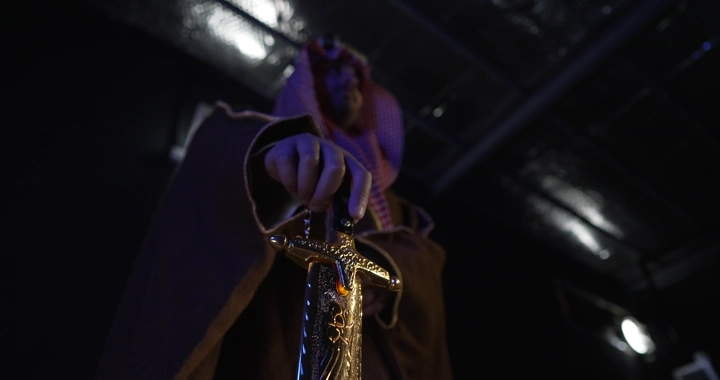 رجل يرتدي بشت ويمسك سيفًا ذهبيًا، لقطة من أسفل.