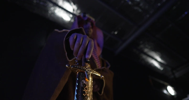 رجل يرتدي زي تقليدي ممسك بسيف في إضاءة خافتة، لقطة منخفضة.