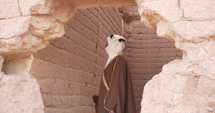 رجل يرتدي الزي التقليدي يقف بين بيوت طينية، لقطة مقربة.