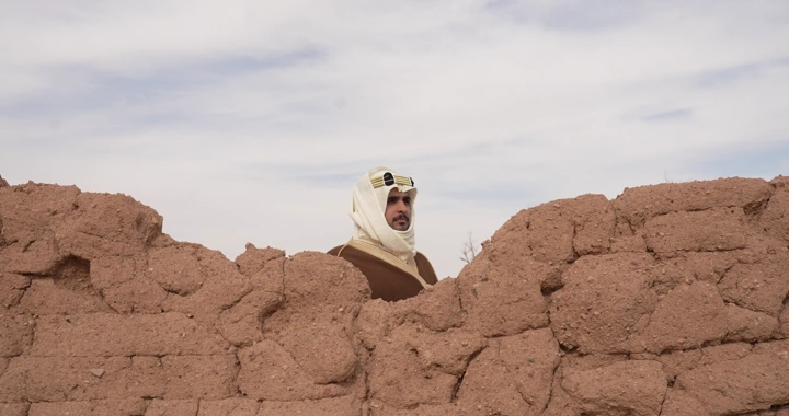 Man in traditional attire standing between mud houses, natural shot.