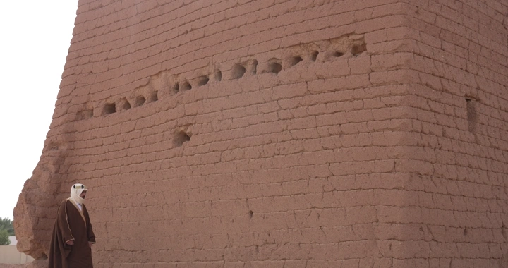 رجل يرتدي ثوبًا تقليديًا بجانب جدار طيني، لقطة أرضية.