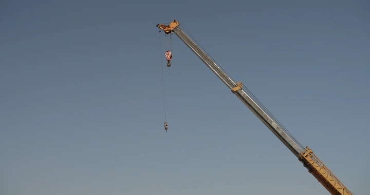 Crane at construction site under blue sky, low-angle shot.