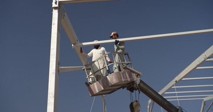 Workers at a construction site under a blue sky, ground shot.