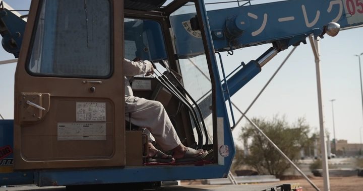 Worker in crane cabin at construction site, side shot.