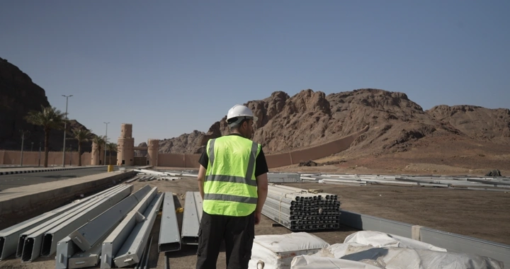 Engineer in safety vest standing at desert construction site, daytime shot.