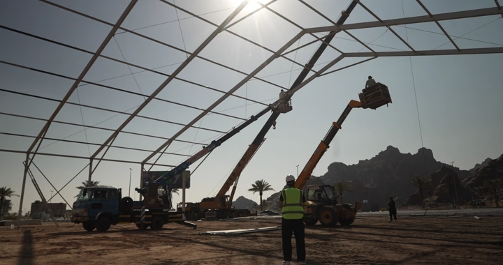 Engineer at construction site with cranes and bright sun, daytime shot.